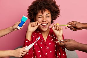 happy curly young woman brushes teeth with tooth floss cares about oral hygiene surrounded with toothpaste electric toothbrush and tongue cleaner 1 - Cuidado e higiene