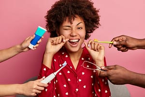 happy curly young woman brushes teeth with tooth floss cares about oral hygiene surrounded with toothpaste electric toothbrush and tongue cleaner 1 - Cuidado e higiene